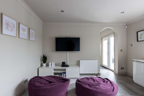 Un salon moderne avec un téléviseur à écran plat fixé au mur, un meuble de rangement blanc et deux fauteuils en forme de poire de couleur violette.