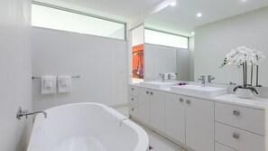 Un baño moderno con una bañera independiente, lavamanos dobles y un espejo grande.