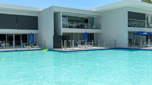 A modern hotel with a large swimming pool, sun loungers, and a glass-enclosed balcony area. - 54 Pool Resort | Port Douglas (PORT DOUGLAS)
