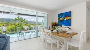 A dining area with a view of a pool and palm trees, a painting on the wall, and a table set for four.