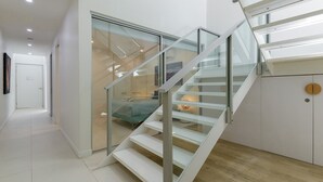 A modern interior with a glass staircase leading to a bedroom with a bed and a nightstand.