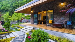 Una casa moderna con fachada de piedra, grandes puertas de cristal y una terraza de madera.