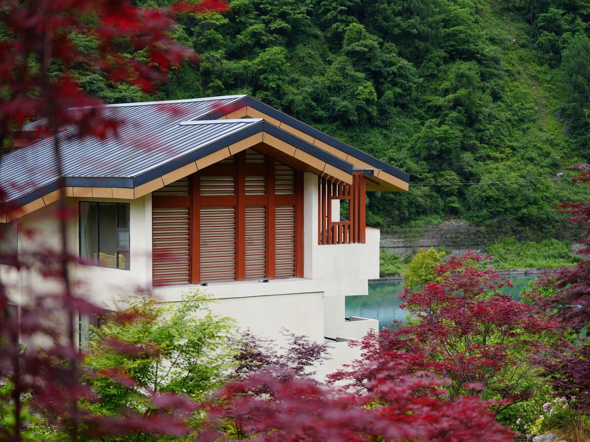 A modern house with a sloped roof, large windows, and a balcony overlooking a lush green landscape.