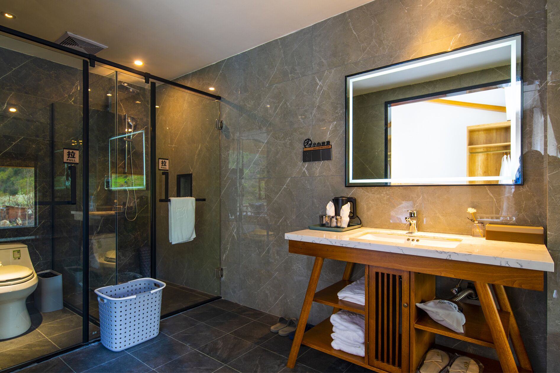Une salle de bain moderne avec une douche à parois de verre, un meuble-lavabo en bois doté d’un grand miroir et un sol carrelé.