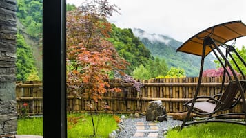 A view through a window of a garden with a bamboo fence, a stone pathway, and a chair with a canopy.
