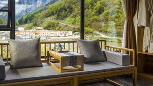 Un balcón con una banca de madera, cojines, una bandeja con tetera y tazas, y una vista panorámica de las montañas.