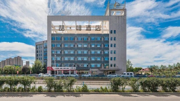 Un hôtel moderne à la façade structurée en forme de grille, avec de nombreux étages et une imposante tour sur le côté droit.