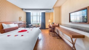 Une chambre d’hôtel avec un grand lit, un bureau, une chaise, un téléviseur fixé au mur et une fenêtre avec des rideaux.