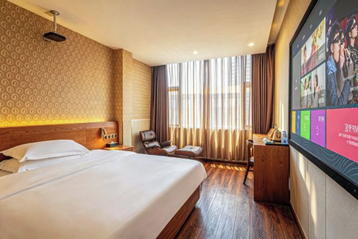 Ein Hotelzimmer mit einem großen Bett, einem Schreibtisch, einem Stuhl, einem Fernseher und einem Fenster mit Vorhängen.