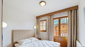 A bedroom with a large bed, a wooden headboard, a nightstand, a window with curtains, and a view of a wooden structure outside. - Grand Lodge GRA13 SPA & MOUNTAIN 6 Pers. (Châtel)