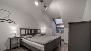 Une chambre à coucher comprenant un lit, des tables de chevet, une lampe suspendue, un radiateur et une armoire.