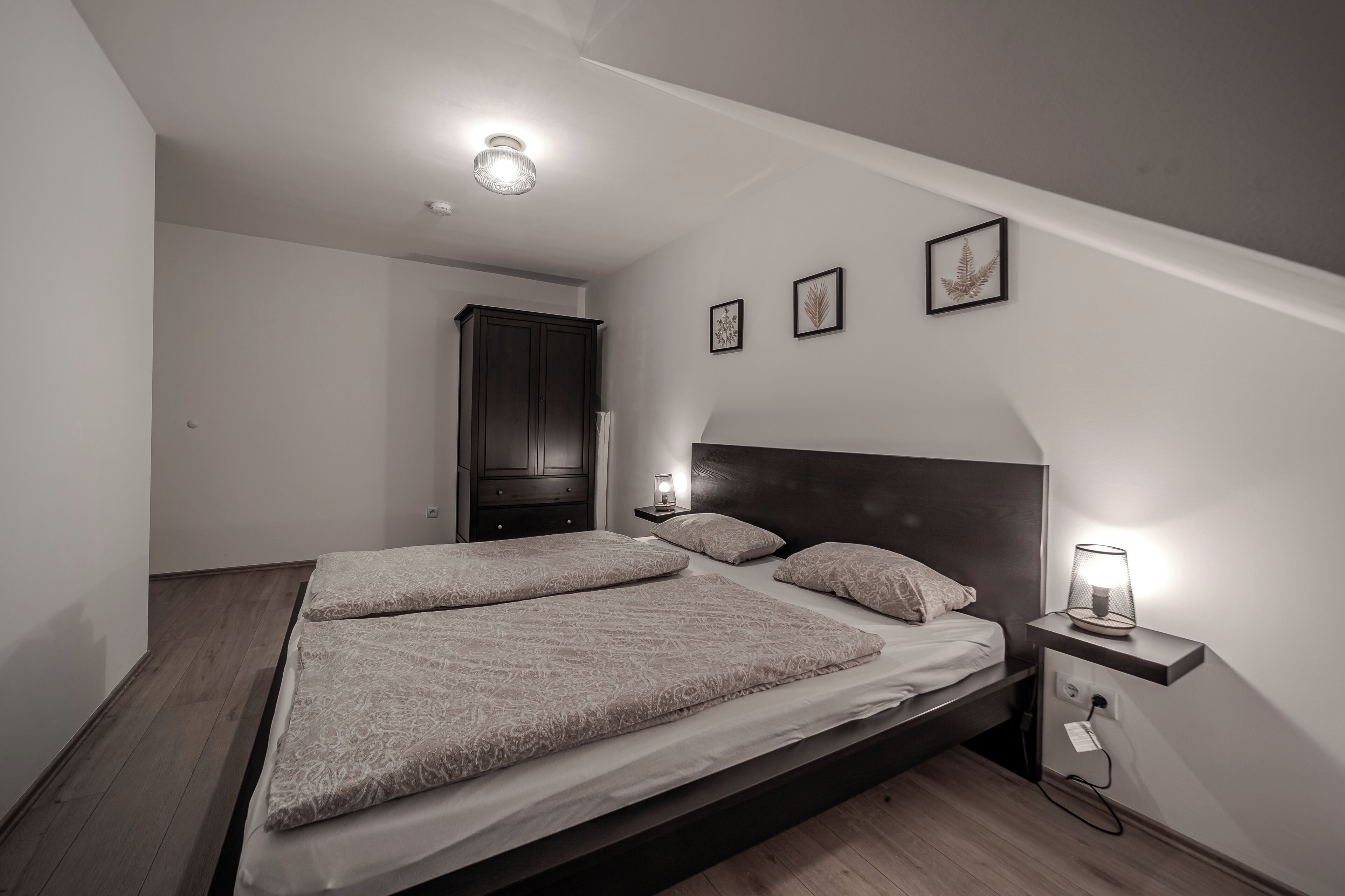 A bedroom with a large bed, a nightstand with a lamp, and a wardrobe.