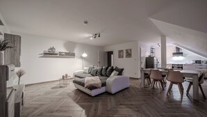 Un salon moderne avec un canapé, une table à manger et des chaises. On aperçoit un coin cuisine à l’arrière-plan.
