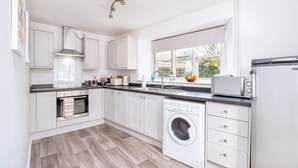 A modern kitchen with white cabinets, a built-in oven, a washing machine, and a window with a view of greenery. - Stone cottage - In the Heart of Stamford (Stamford)