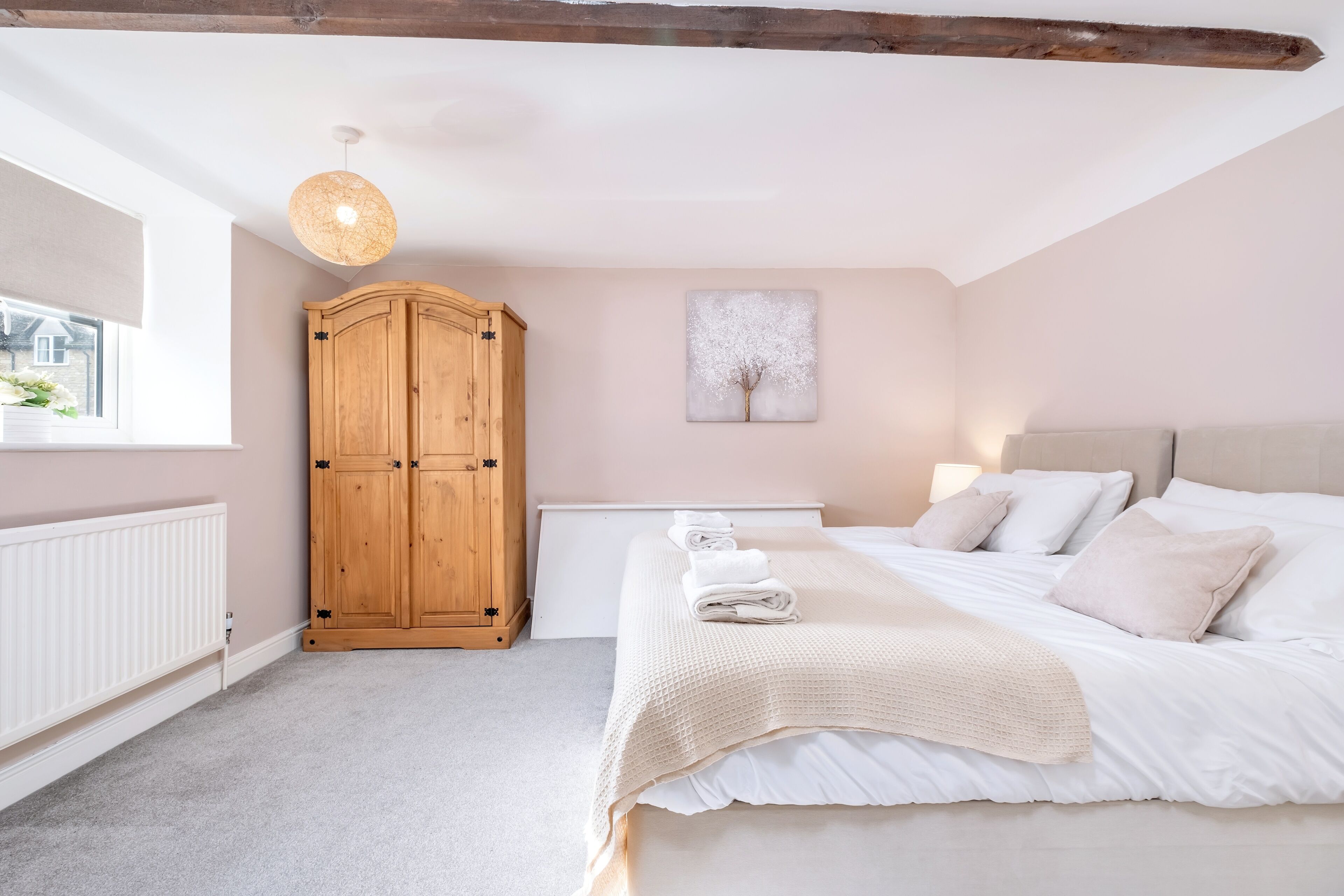 A bedroom with a bed, a wooden wardrobe, a radiator, and a window.