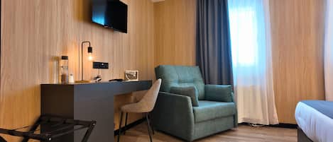 Una habitación de hotel moderna con una pared de madera, un televisor de pantalla plana sobre un escritorio, un sillón verde, una mesita de noche con una lámpara y una cama con cabecera blanca.