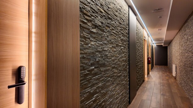 A hallway with a wooden door on the left and a textured stone wall on the right.