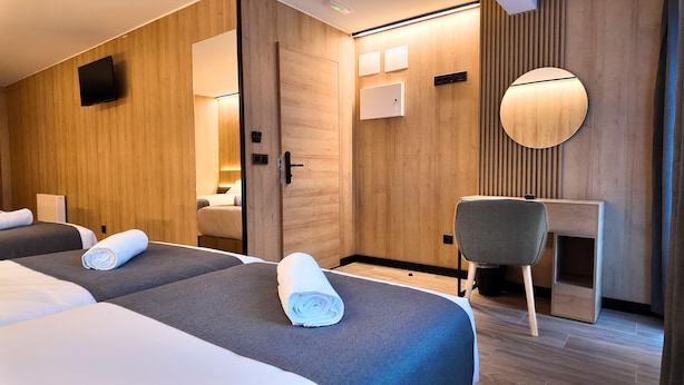 Ein Hotelzimmer mit zwei Betten, einem Schreibtisch, einem Sessel, einem Fernseher und einem Spiegel.