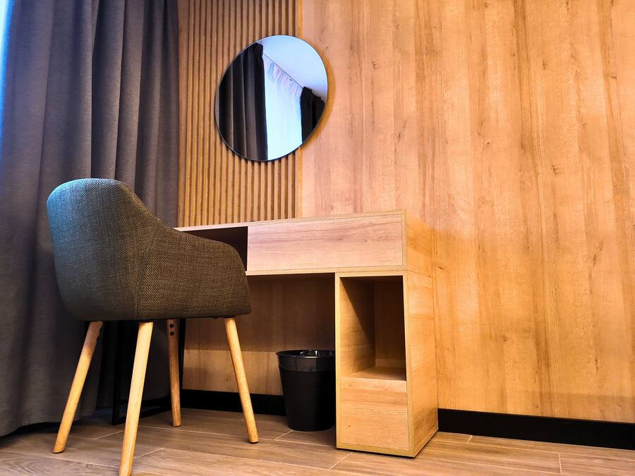 A room with a wooden desk, a chair, a mirror, and a black trash bin.