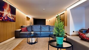 Ein modernes Wohnzimmer mit einem grauen Sofa, einem kleinen runden Tisch, einer Topfpflanze und einem Kamin mit Feuer.