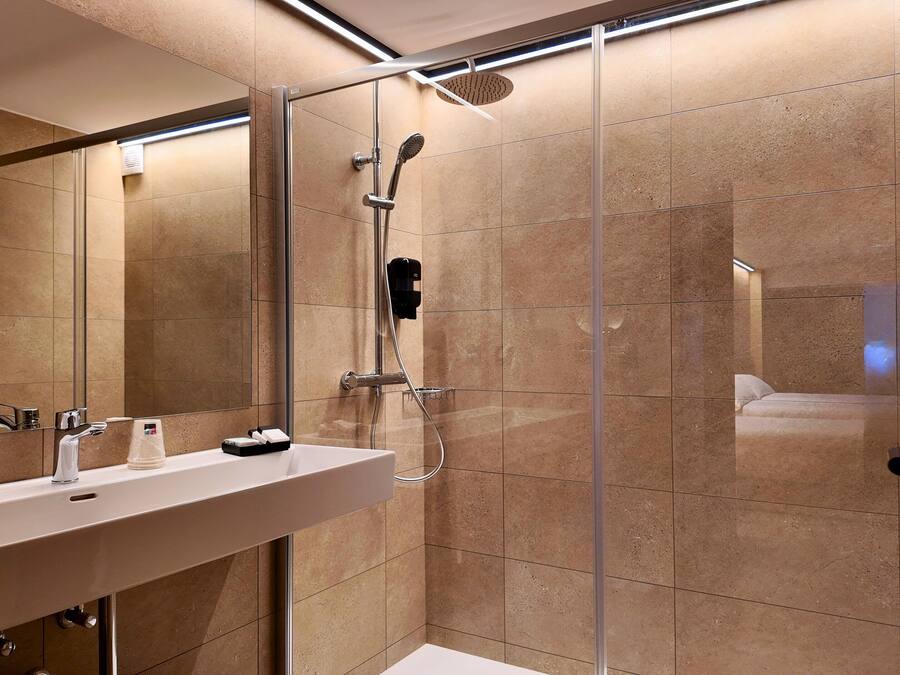 A modern bathroom with a glass-enclosed shower, a large mirror, and a white sink.