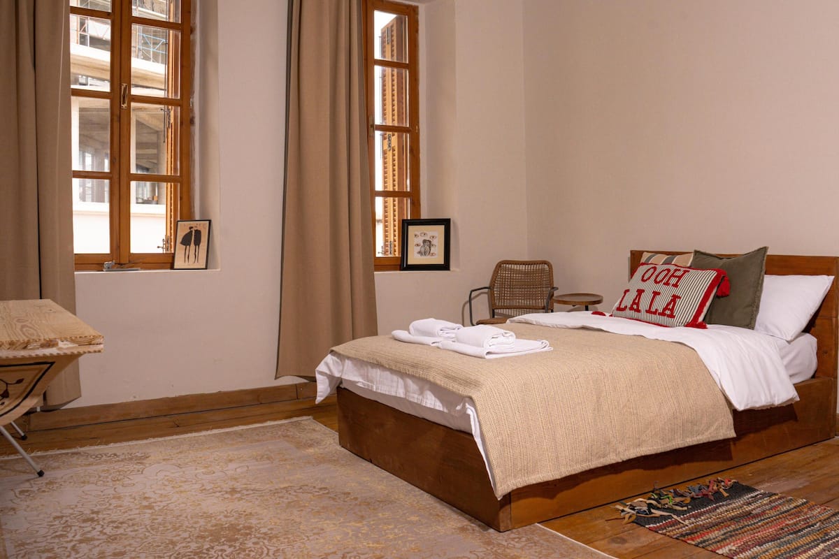 A bedroom with a wooden bed, a chair, a small table, and a window with curtains.