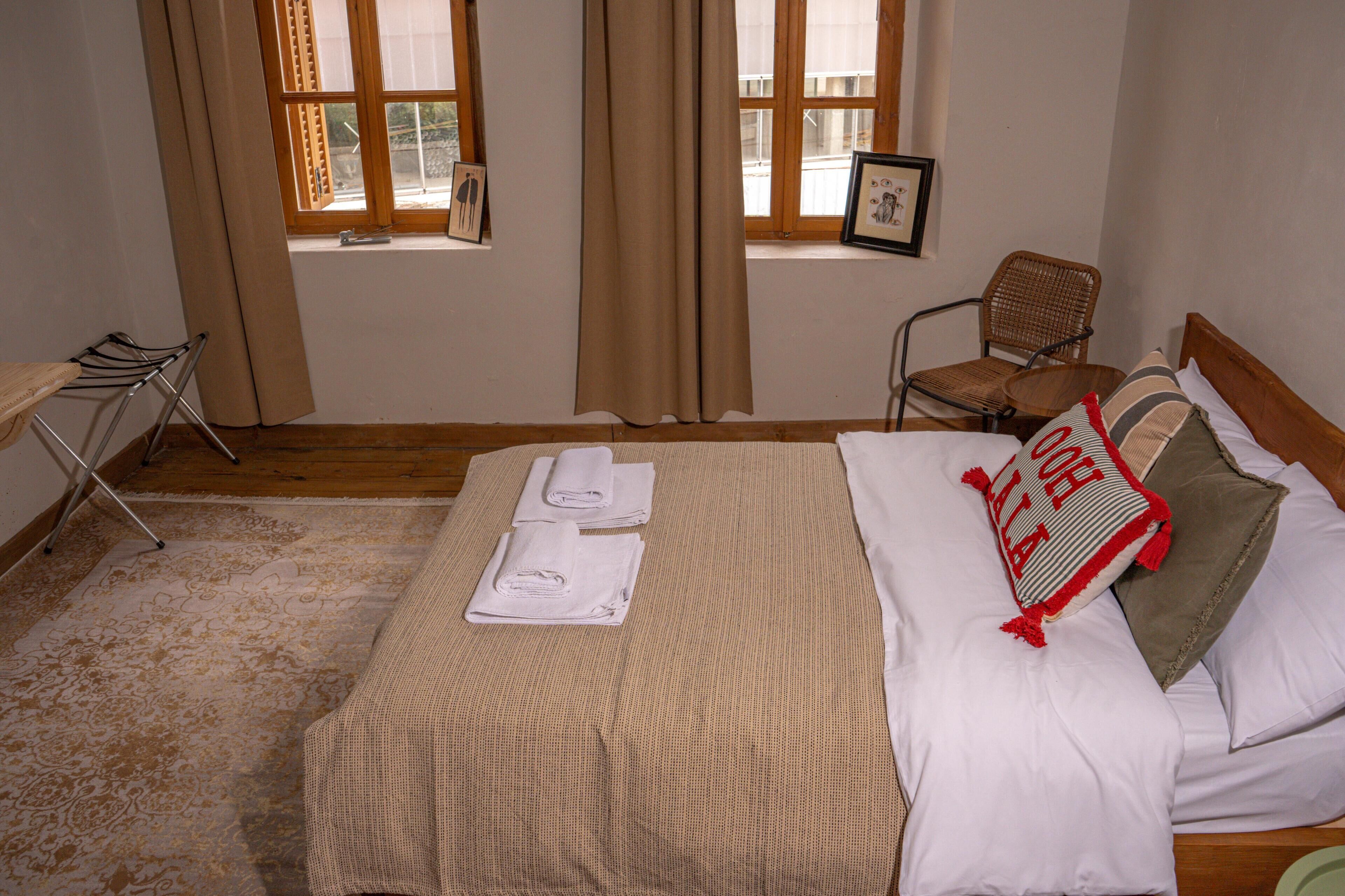 A neatly made bed with white linens and a striped pillow, a chair, and a window with curtains.