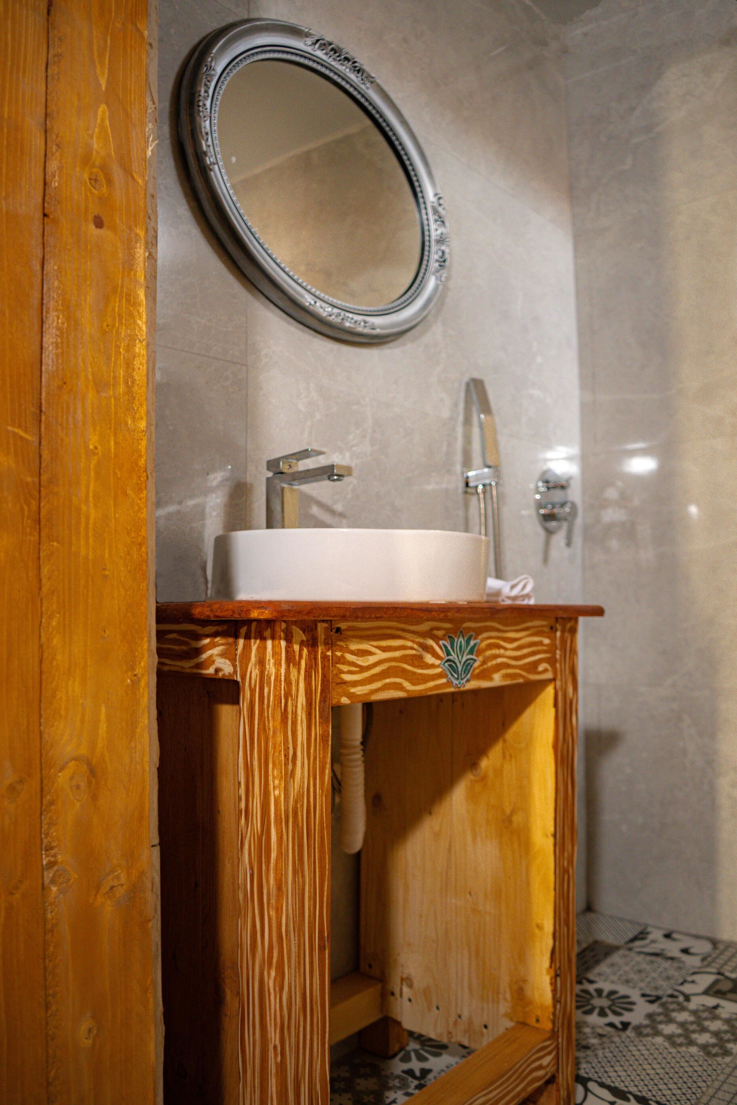 Ein Badezimmer mit einem Holzwaschtisch, einem weißen Waschbecken, einem Spiegel und einer Duschkabine.