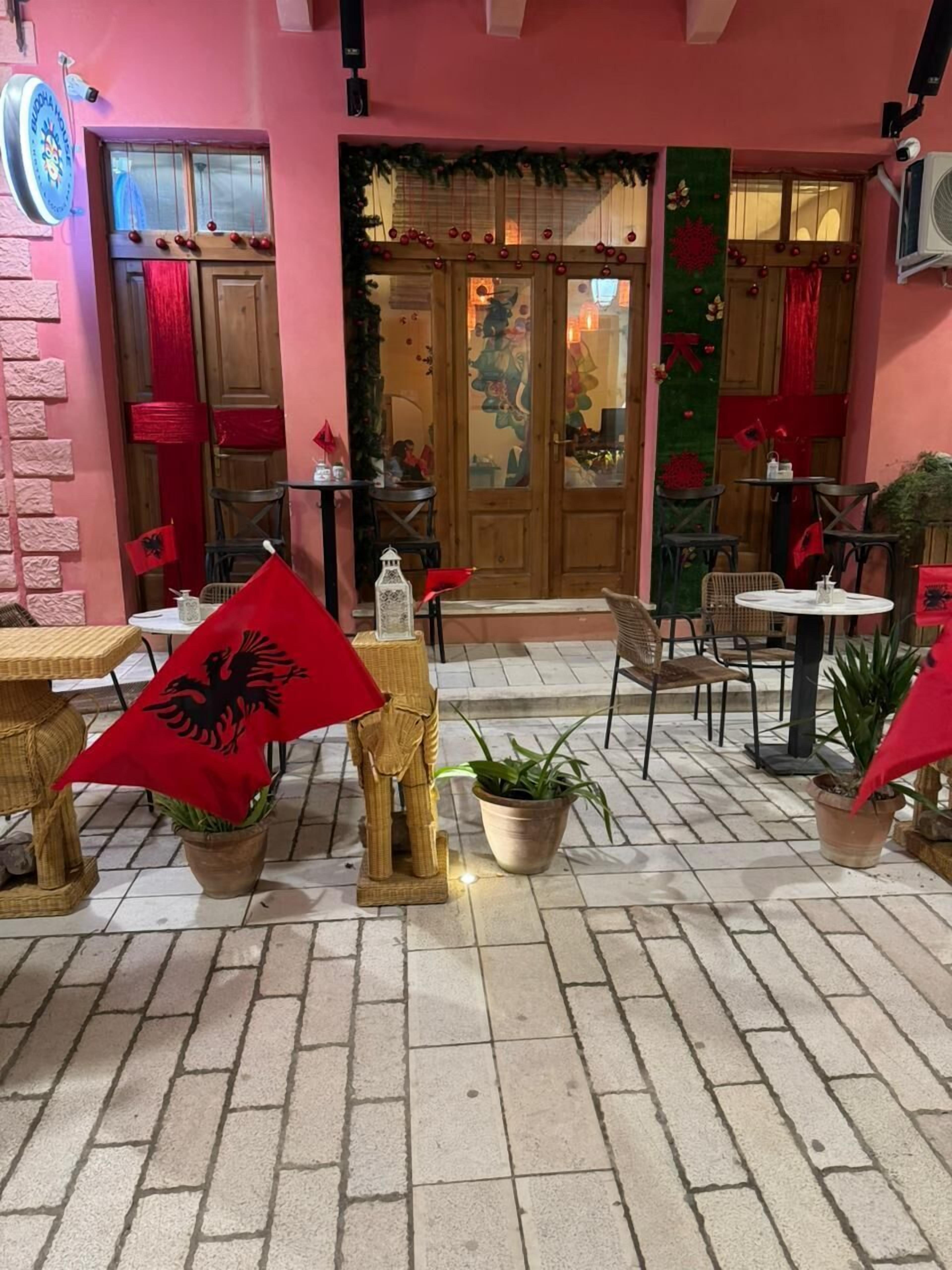 Een terras met tafels en stoelen, potplanten en een decoratieve ingang met een houten deur en glaspanelen.