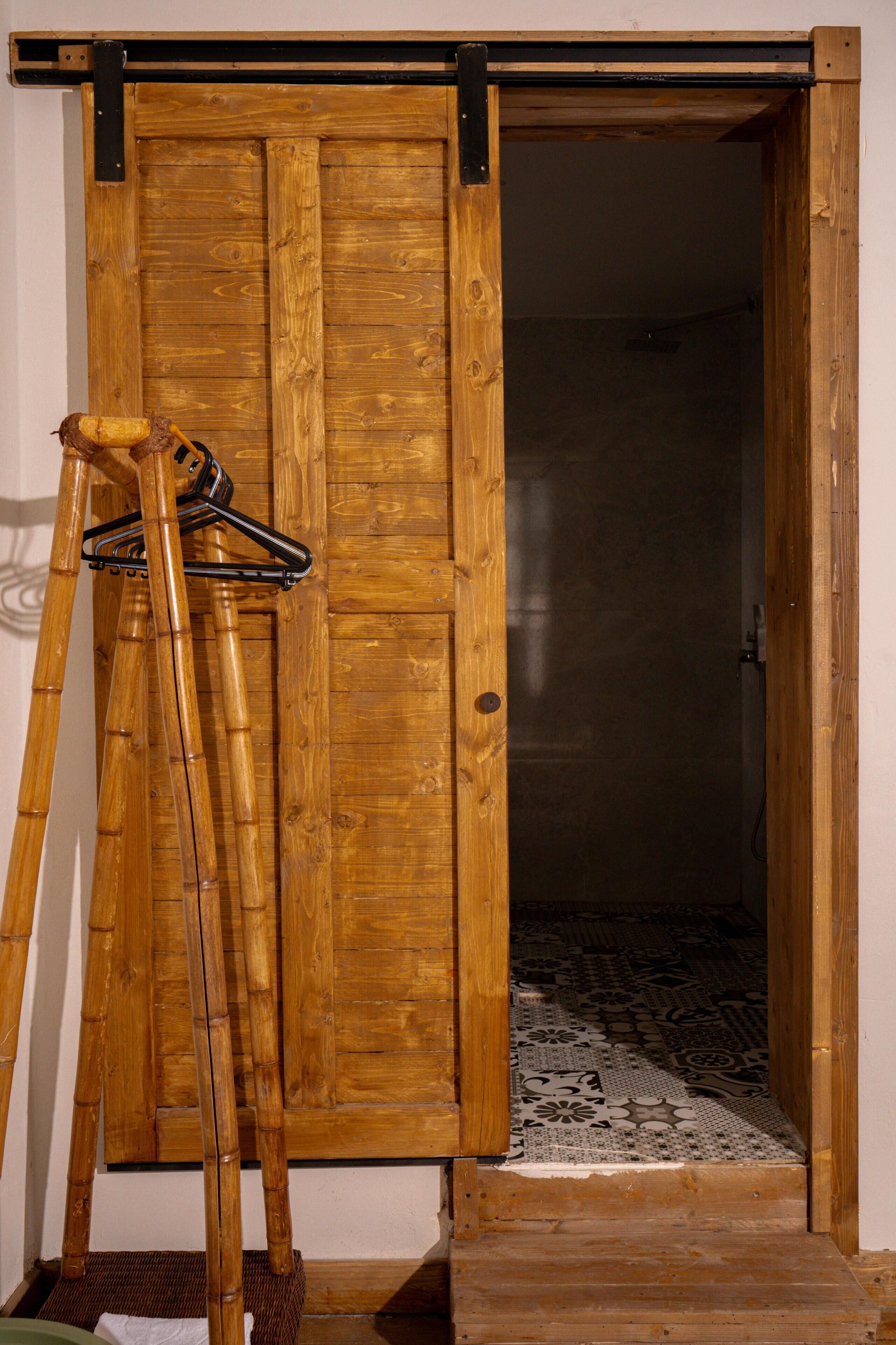 Una puerta de madera con un picaporte metálico y una escalera de bambú apoyada en ella.