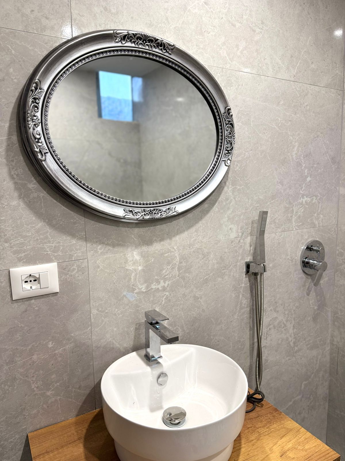 A bathroom with a round mirror, a white sink, and a handheld showerhead.