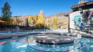 Un espace piscine comprenant un jacuzzi, des chaises longues et un panneau indiquant que la piscine et le jacuzzi sont accessibles 20 heures par jour.