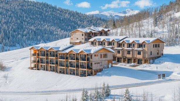 Un chalet en bois à plusieurs étages, doté de balcons, situé dans une région montagneuse enneigée.