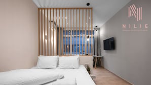 A modern hotel room with a large bed, a TV mounted on the wall, and a view of the city through large windows.