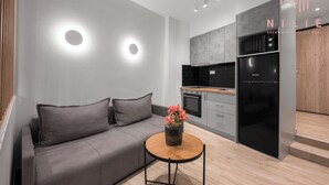 A modern kitchen with a grey sofa, a small round table with a vase of flowers, and a built-in oven.