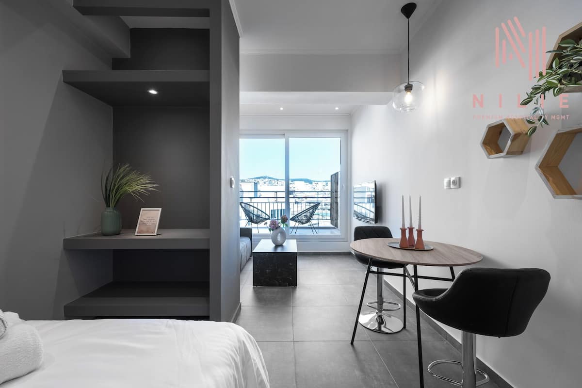 Une chambre d’hôtel moderne comprenant un lit, un coin repas avec une table et des chaises, un escalier et une vue sur la ville grâce à de grandes fenêtres.