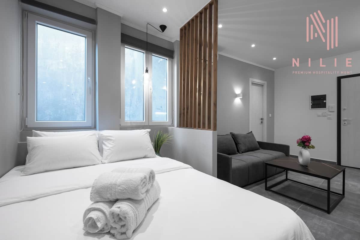 Une chambre d’hôtel moderne avec un grand lit, un canapé et une petite table. On peut voir des fenêtres et une porte.