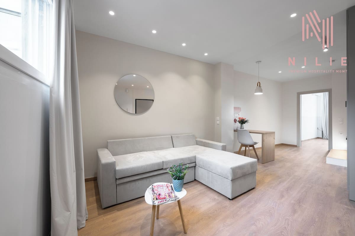 Un salon moderne avec un canapé d’angle gris, un miroir rond, une petite table avec une plante et un plancher en bois.