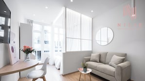 A modern living room with a sofa, a round mirror, a small table with a vase, and a dining area with a chair and a table.
