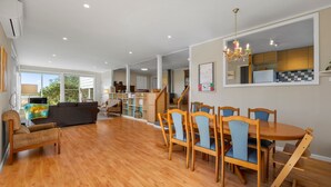 A spacious living area with a wooden dining table and chairs, a sofa, and a staircase leading to an upper floor. - Pelican Point- Located next to Edwards Point Wildlife Reserve (St Leonards)