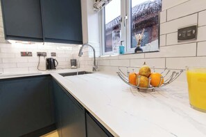A kitchen with a white countertop, a sink, a window with a view, and a fruit bowl with oranges. - Charming Home in Bromsgrove: Perfect for Groups (Birmingham)