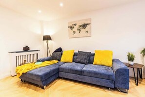 A living room with a sectional sofa, a world map on the wall, a lamp, and a small table with a plant. - Charming Home in Bromsgrove: Perfect for Groups (Birmingham)
