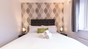 En snyggt bäddad säng med hoprullade handdukar, en sänggavel med mönster och sänglampor.