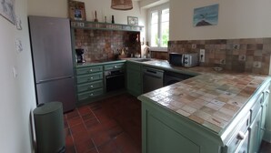 A kitchen with green cabinets, a tiled backsplash, a microwave, and a hanging light fixture.