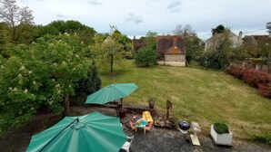 A backyard with a grassy lawn, a stone wall, and a small garden area with a barbecue grill and potted plants.