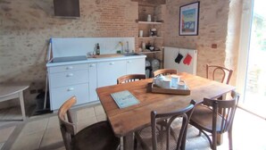 Een rustieke keuken met een houten tafel, witte kasten en een bakstenen muur.