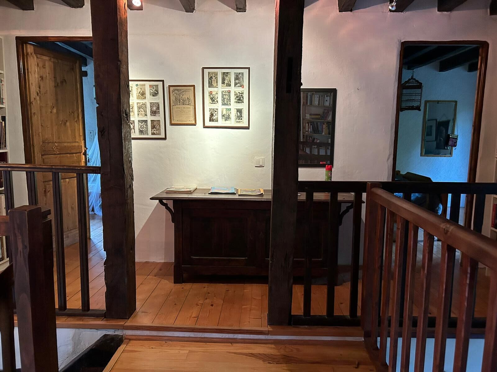 A wooden staircase leading to a room with a desk, framed pictures on the wall, and a bookshelf.