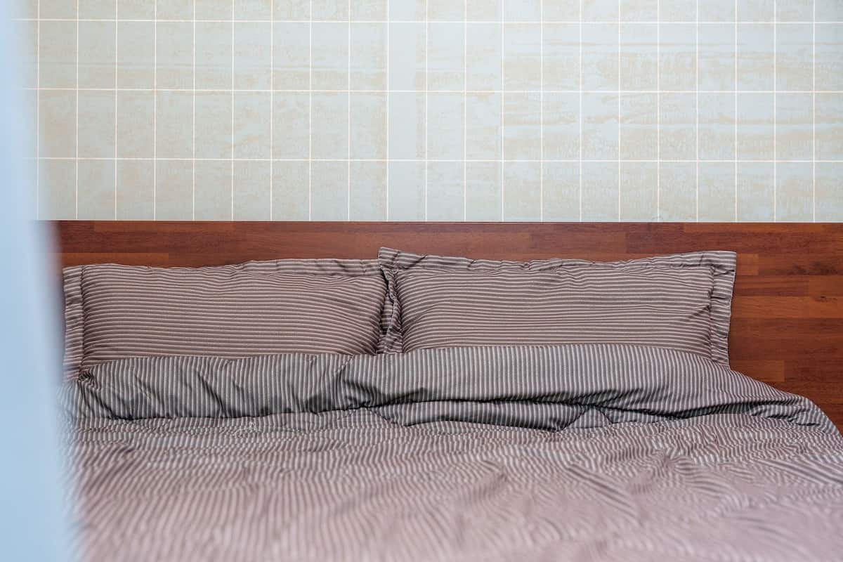 Een bed met gestreept beddengoed en een houten hoofdeinde in een kamer met betegelde muren.