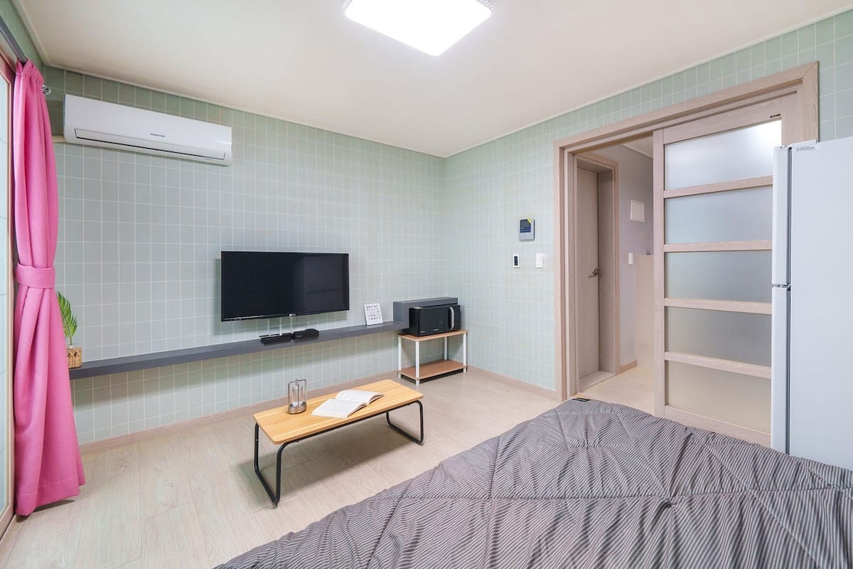 Een kleine, goed verlichte kamer met een televisie, een magnetron, een tafeltje en een bed.