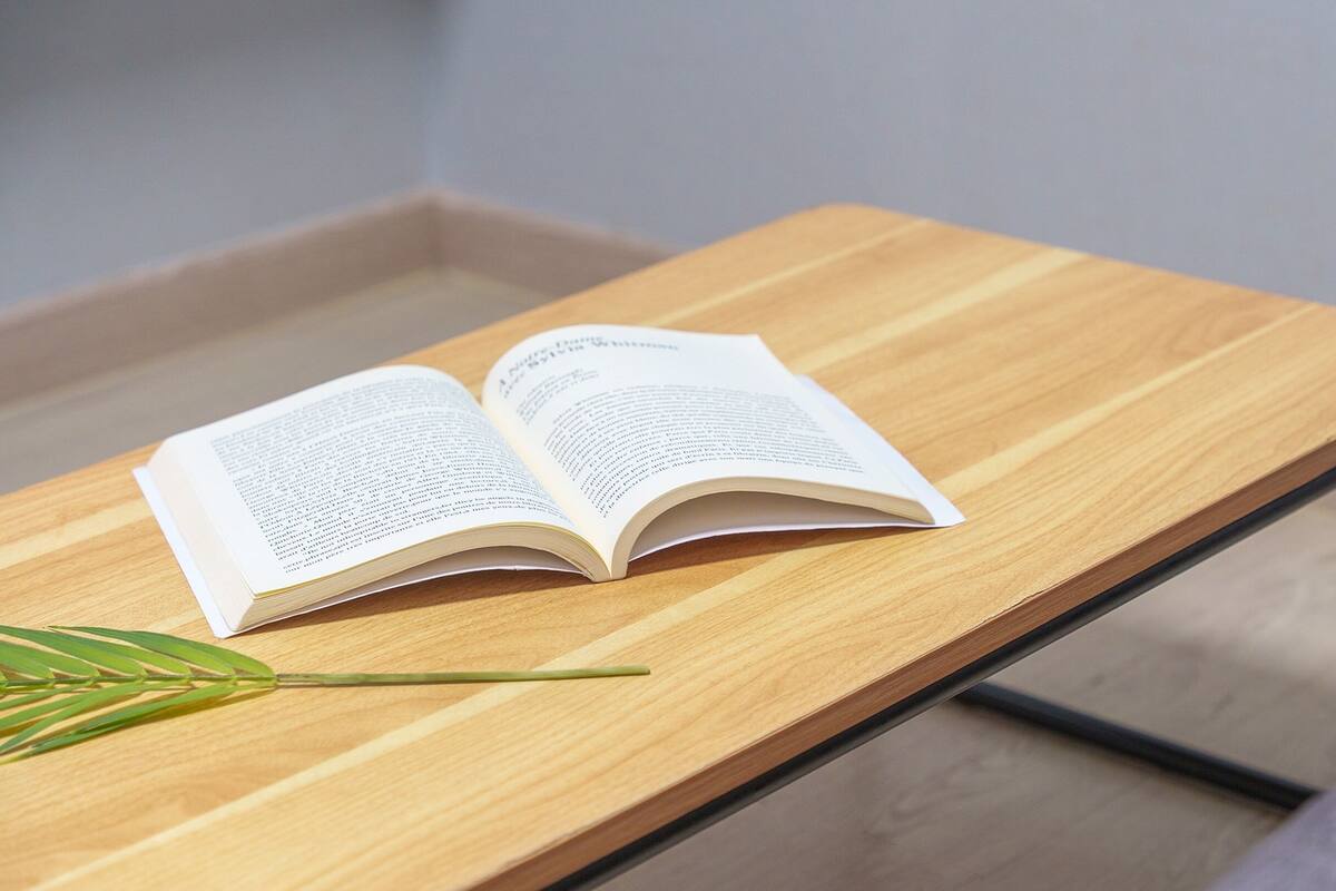 Een open boek op een houten tafel met een metalen frame.